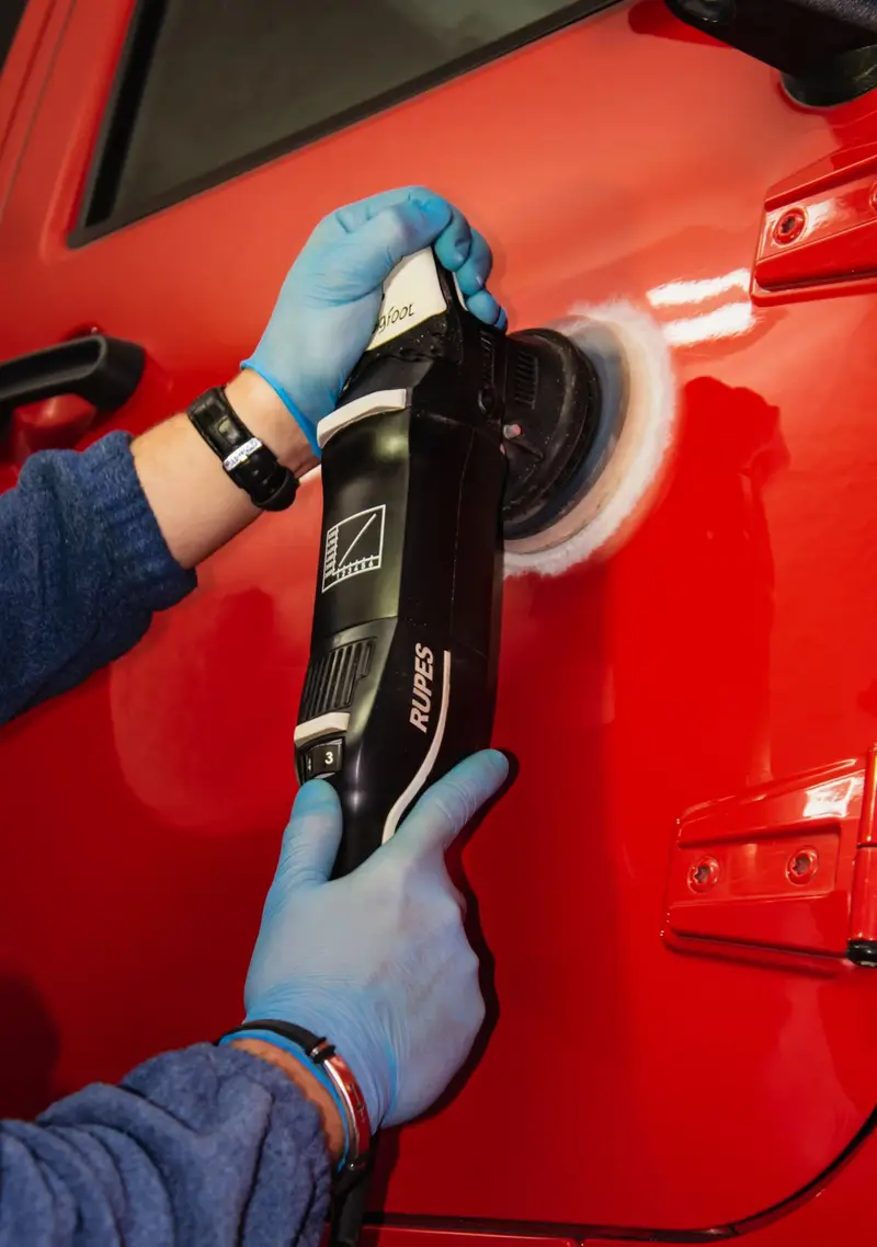 Gloved hands guiding a machine polisher across a red car door