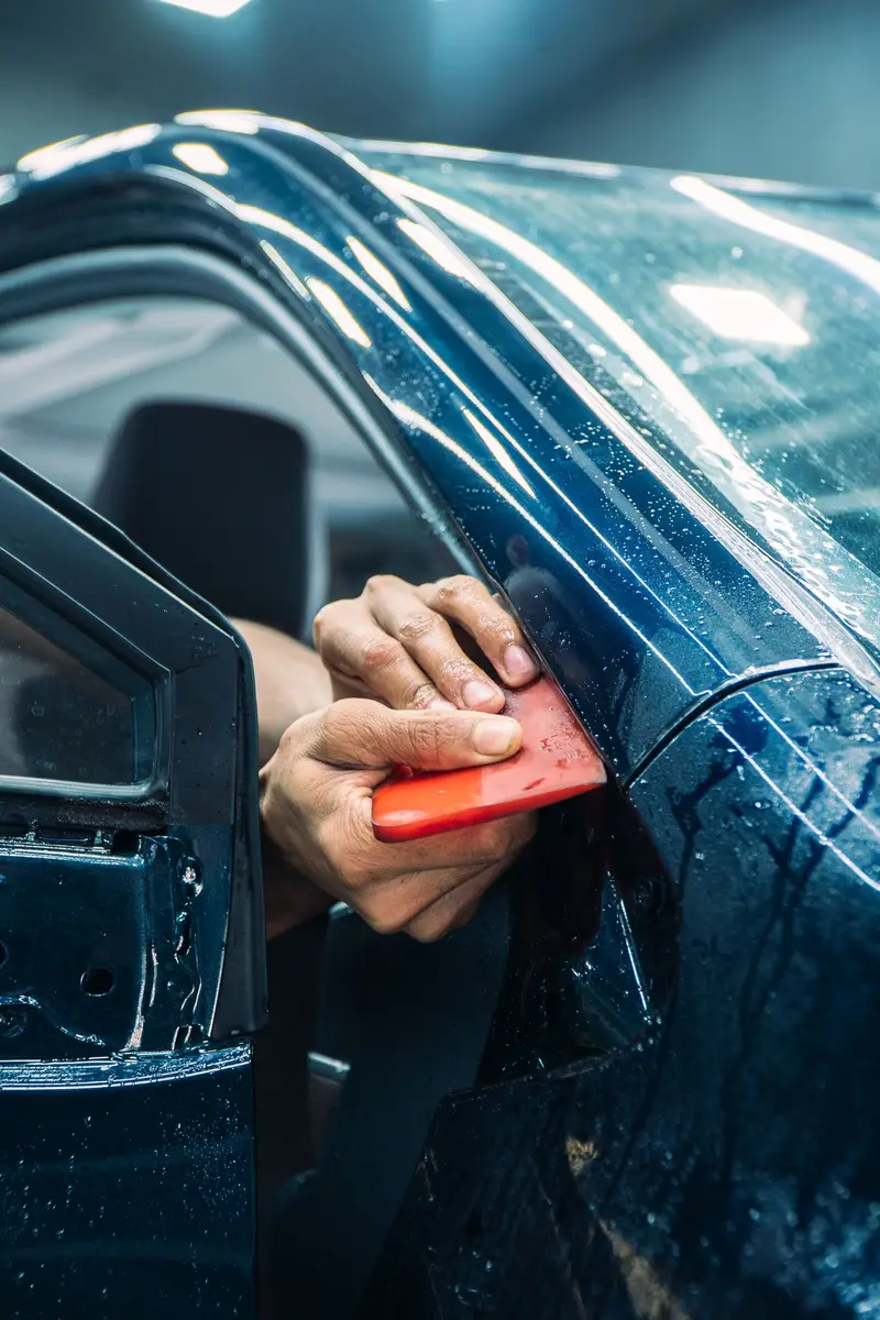Squeegee pressing film down along the edge of a dark blue car door