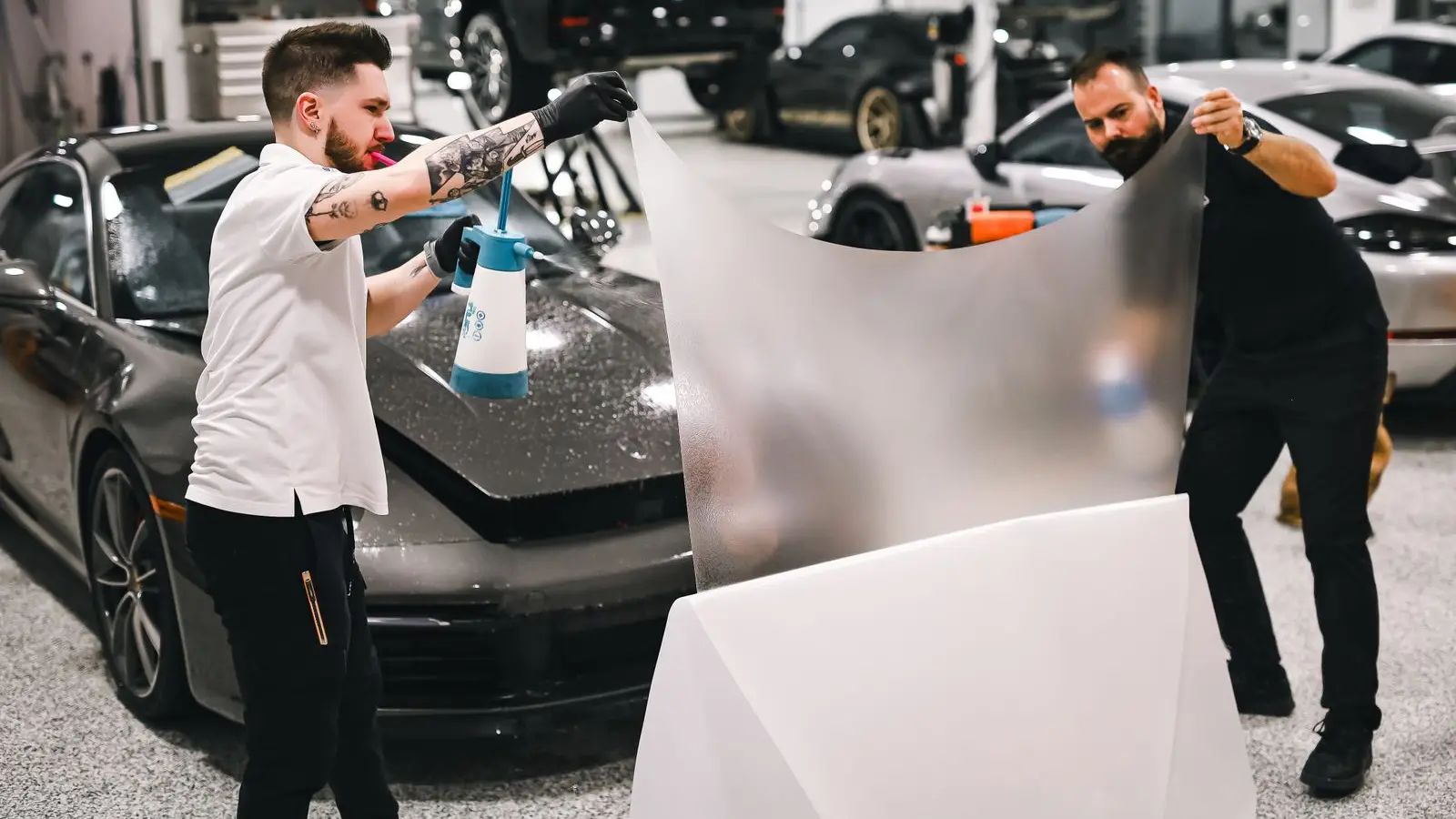 Installers laying clear film over the front of a sports car in a workshop